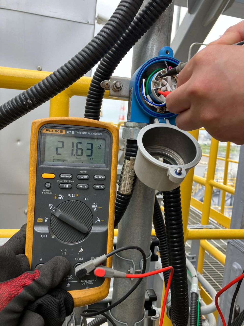 Mesure au multimètre sur un équipement d’instrumentation, avec les mains de l’intervenant visibles.
